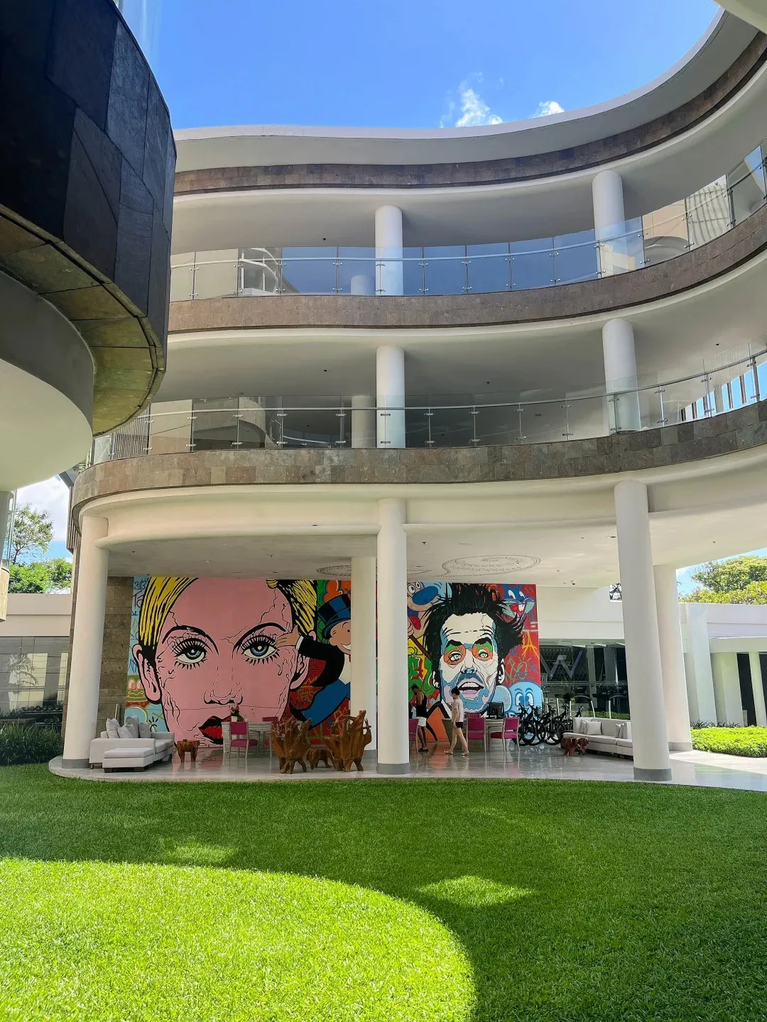 Pop-art murals under the hotel’s curved white balconies, behind a lawn