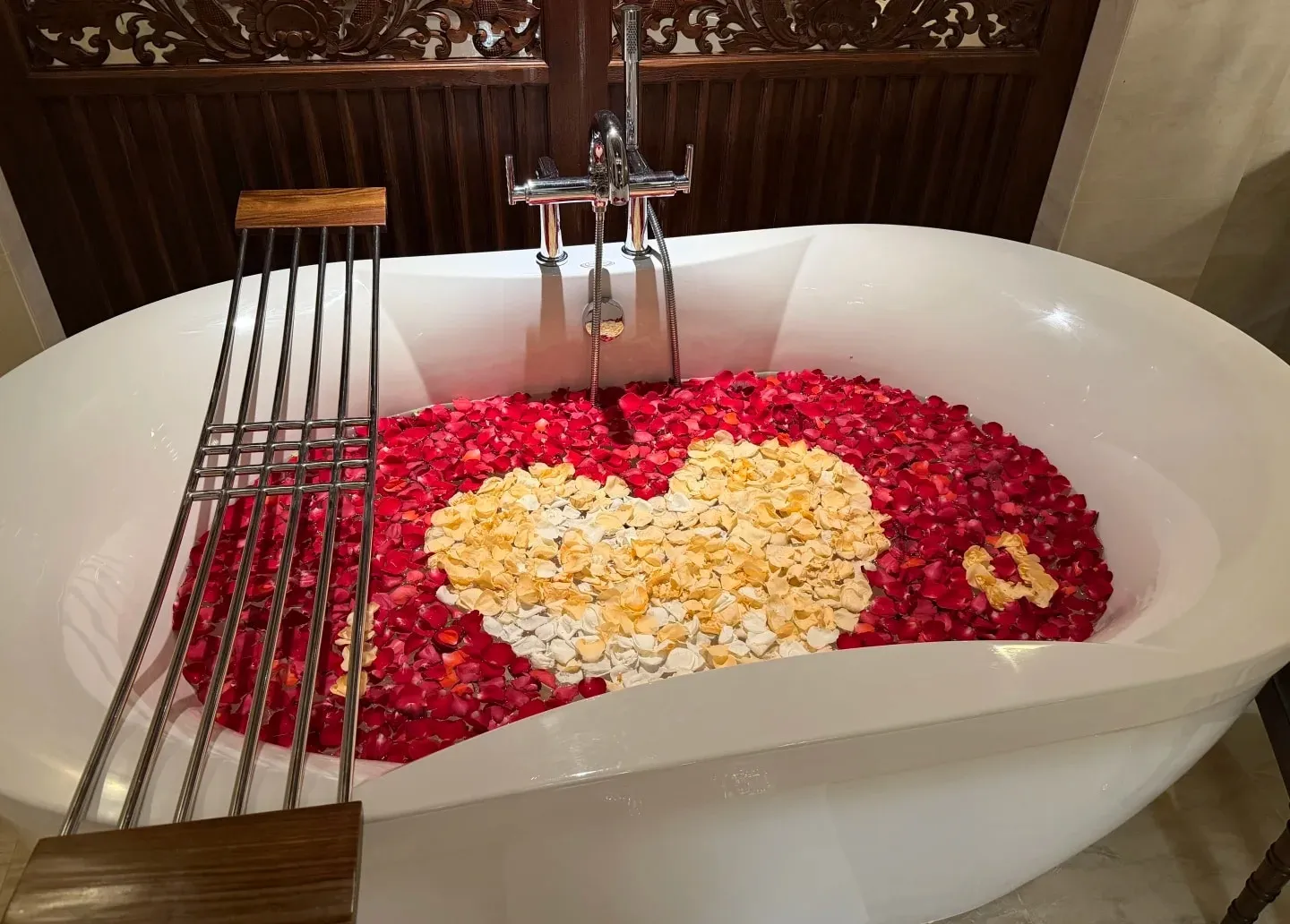 A freestanding bathtub filled with red and white petals laid out in a heart
