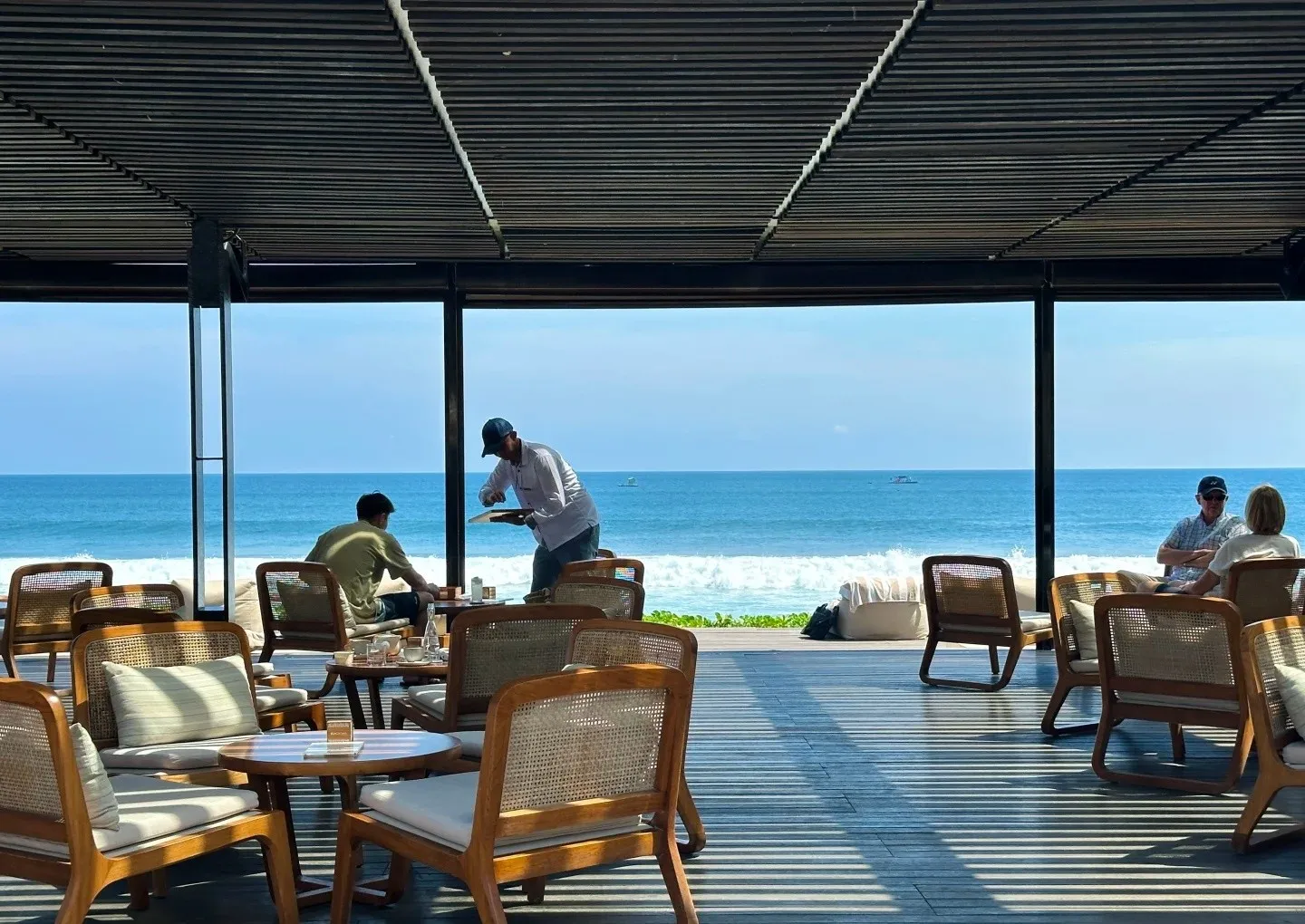Rattan chairs and tables under a timber roof, open to the beach and the surf