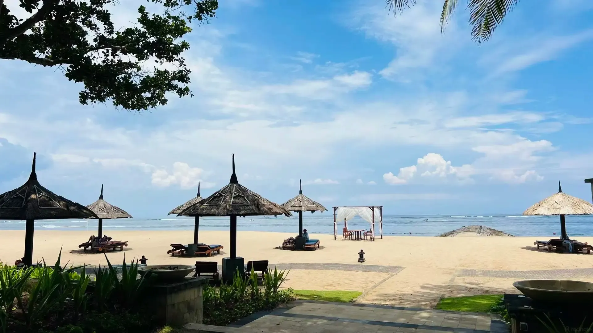 Thatched umbrellas and loungers on the sand in front of calm water
