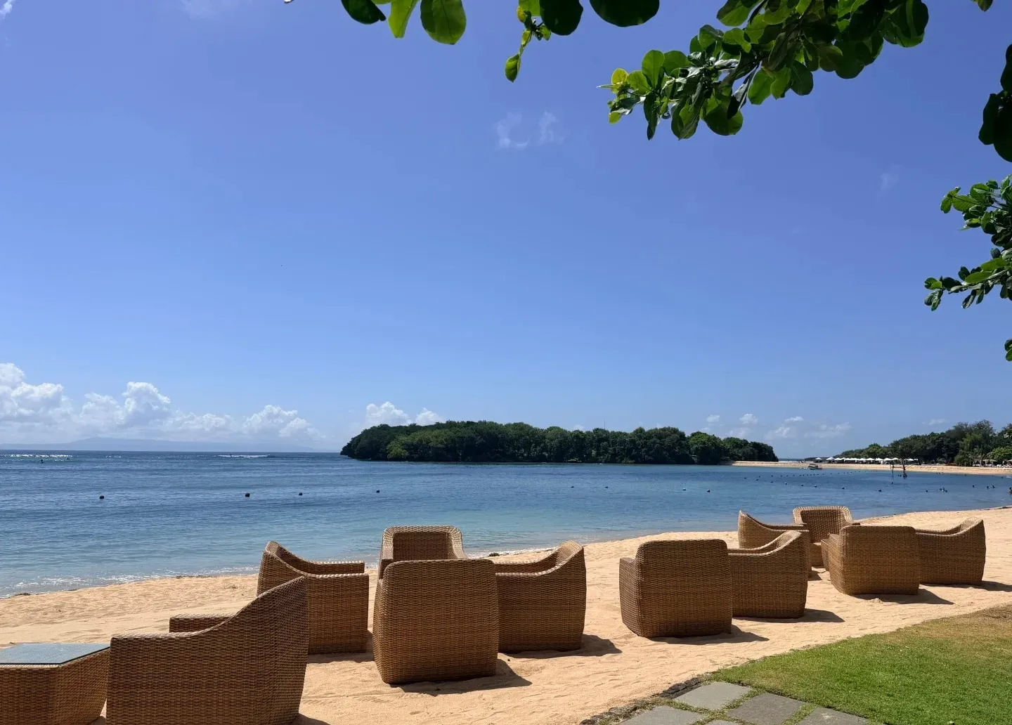 Rattan loungers on the sand facing calm water and a small island off Nusa Dua