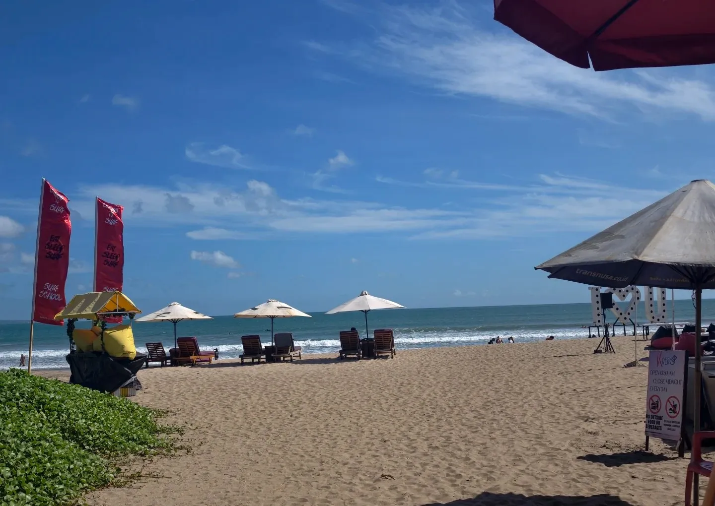 Umbrellas and sun loungers on the wide sand of Seminyak beach under a blue sky