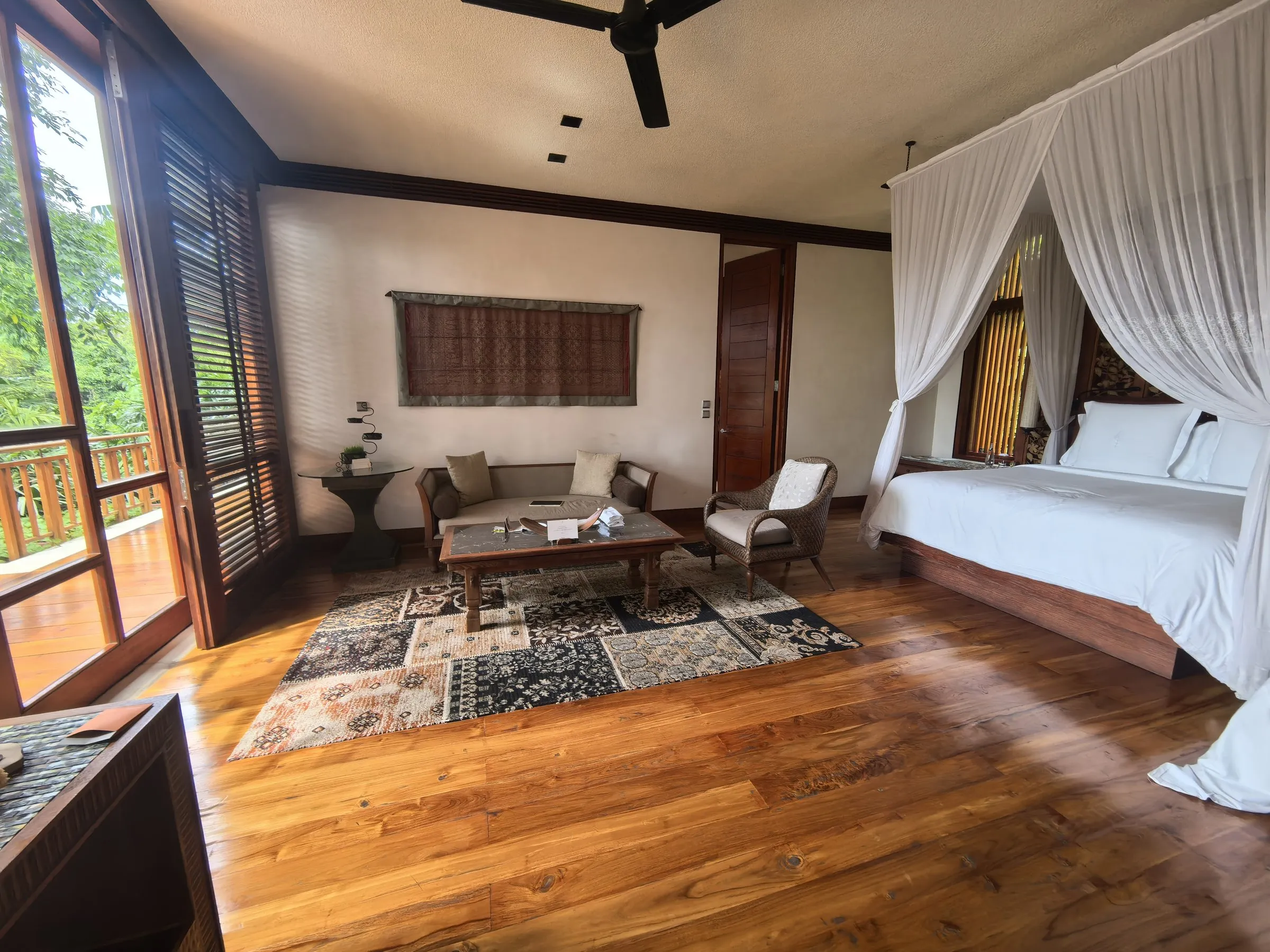 A suite bedroom with a canopy bed, timber floors, a Persian rug and shuttered windows onto the trees