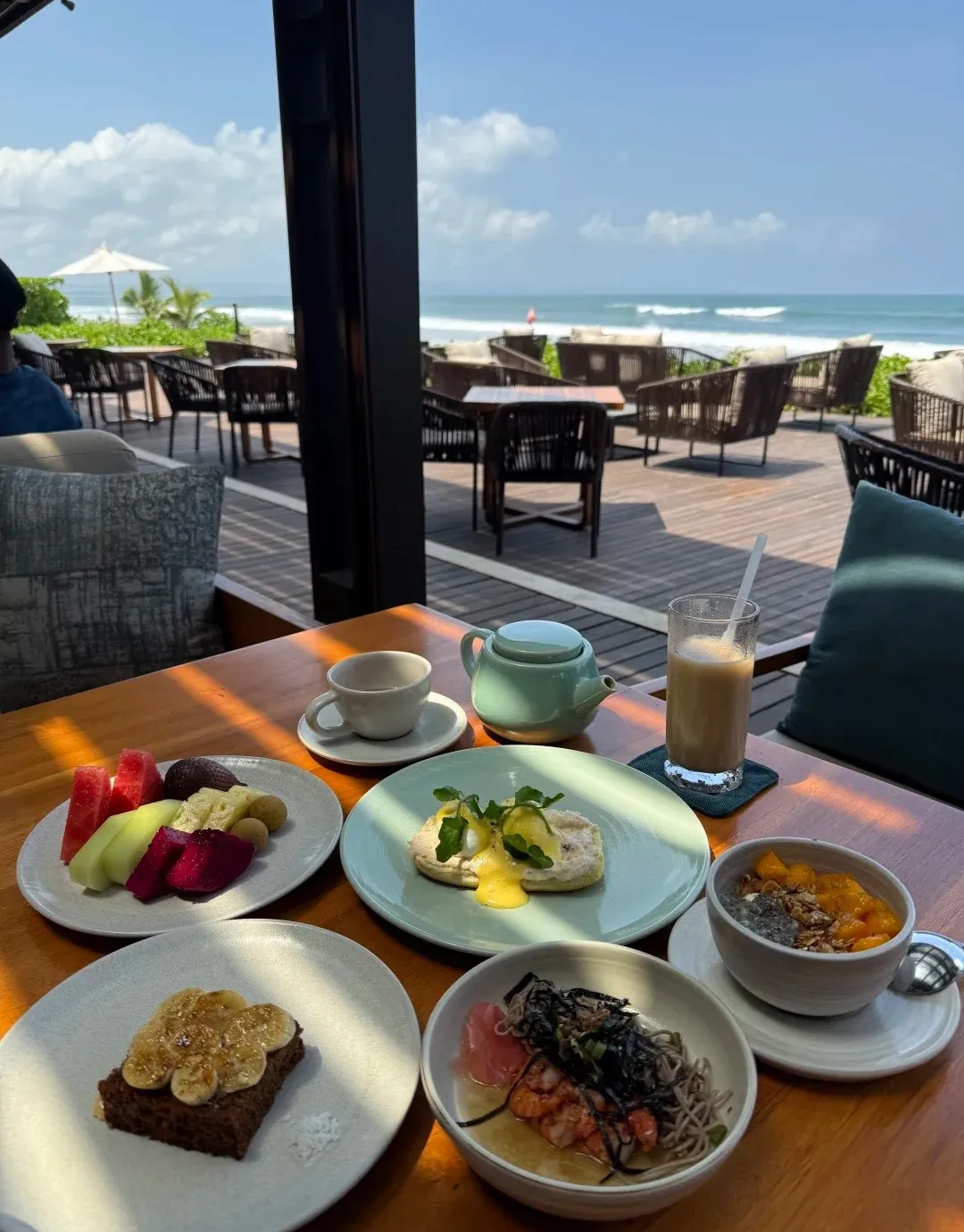 Breakfast of fruit, avocado toast, a smoothie bowl and coffee on a terrace above the beach