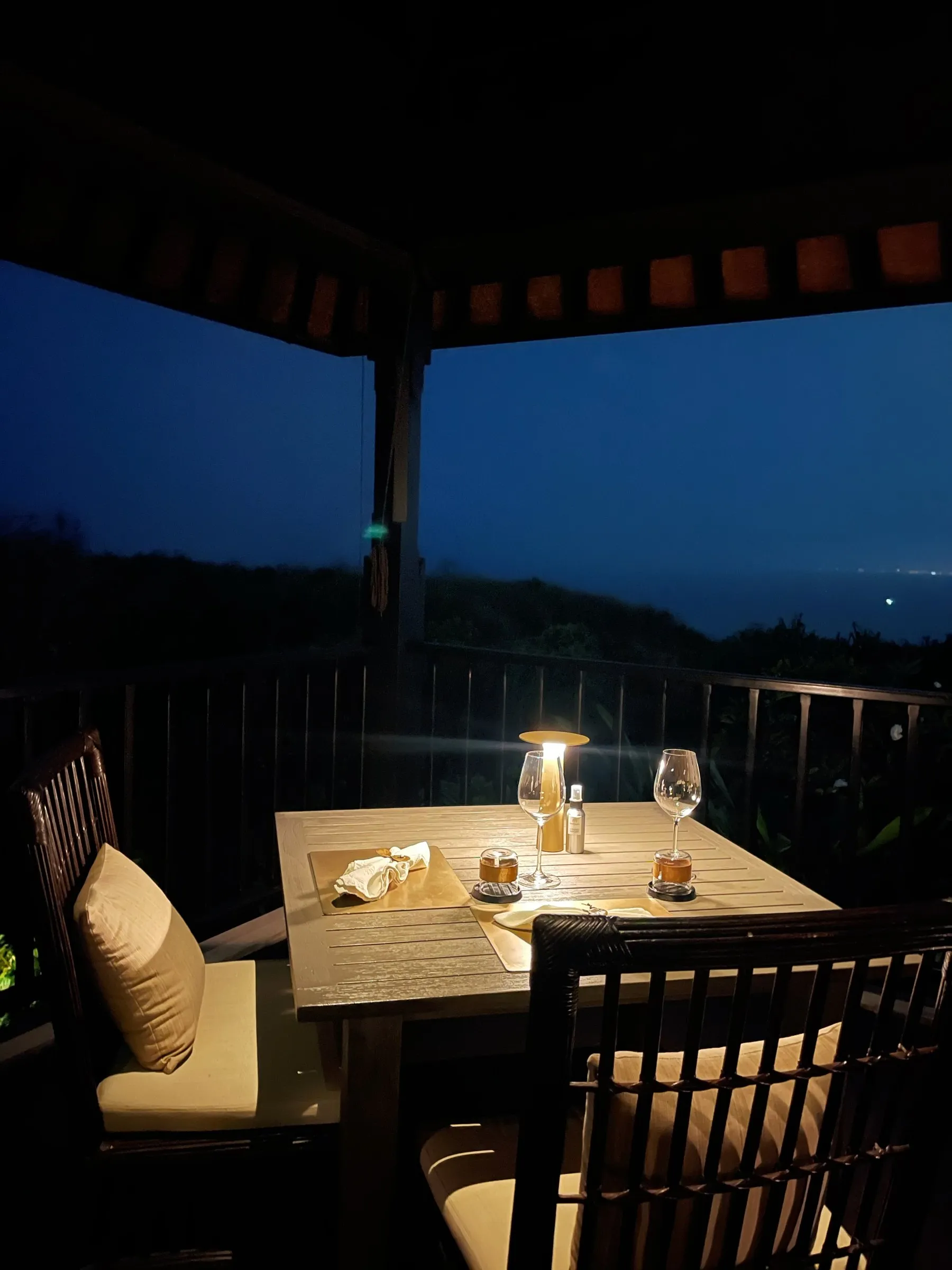 A candlelit table for two on a covered terrace above the bay at dusk