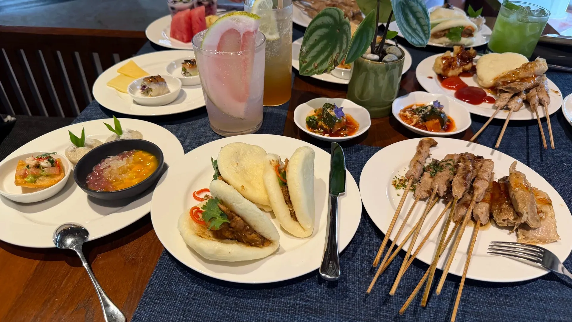 Bao buns, satay skewers, small plates and iced drinks spread across a table at the Grand Hyatt
