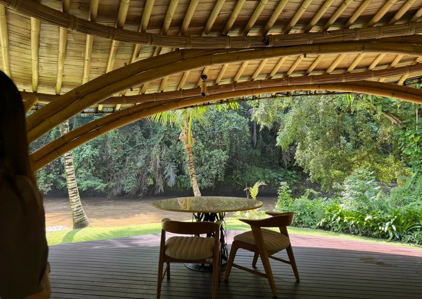 A table for two under a curved bamboo roof, looking out to the river and jungle
