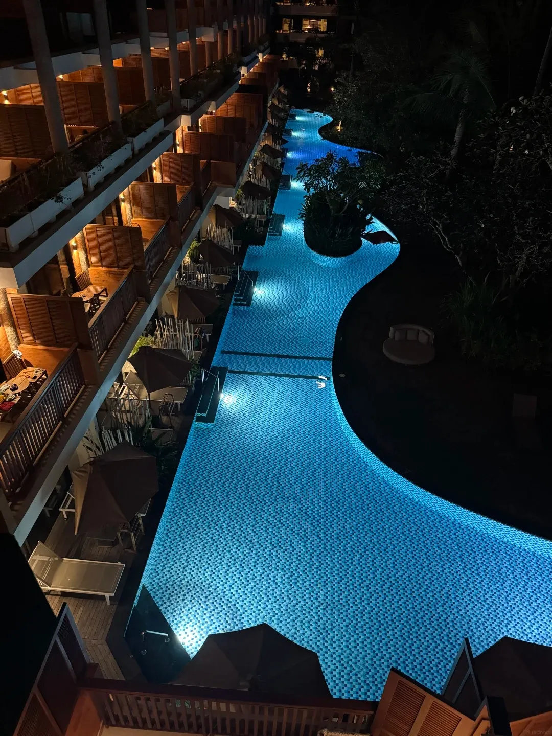 A lit lagoon pool running below the guest wing balconies at night