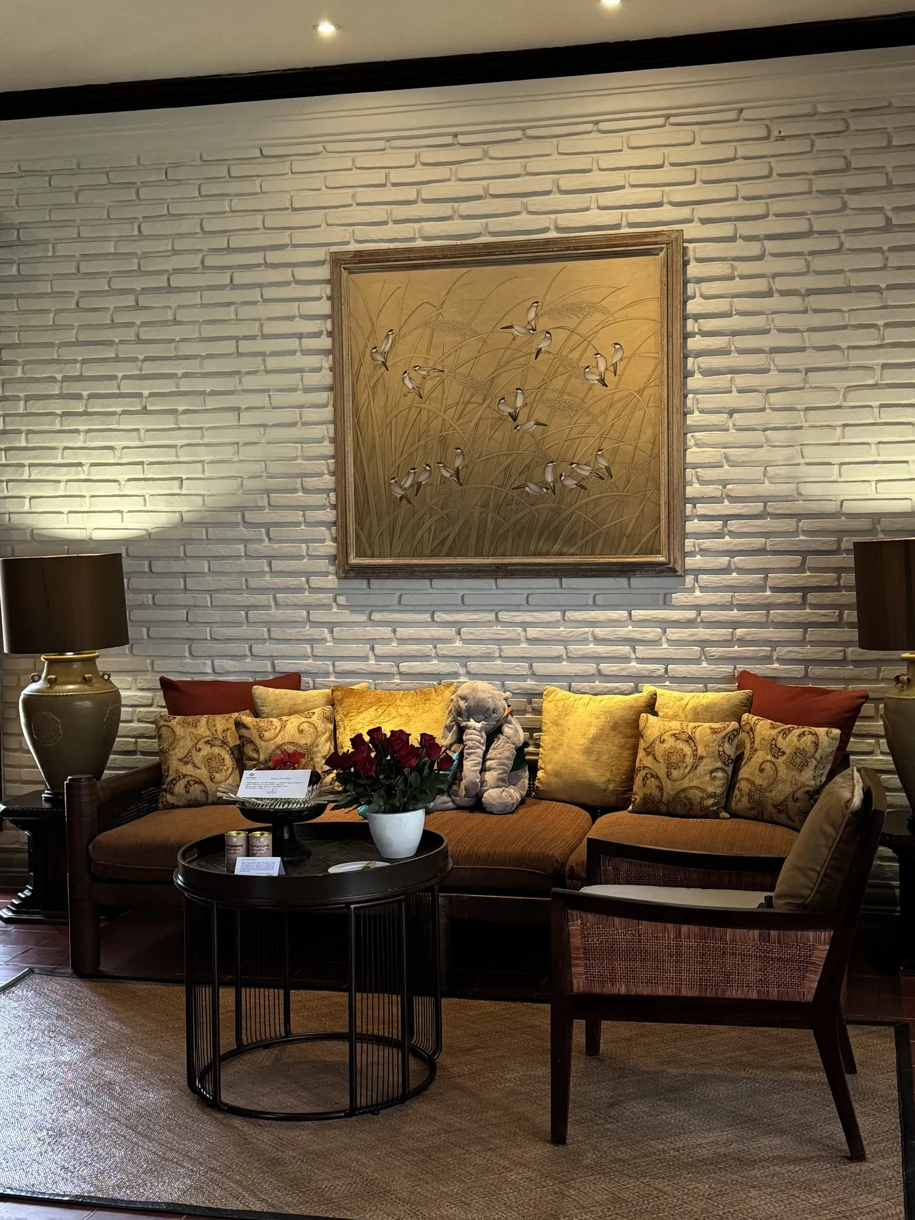 A suite sitting room with a deep sofa and gold cushions, under a painting of birds on a white brick wall