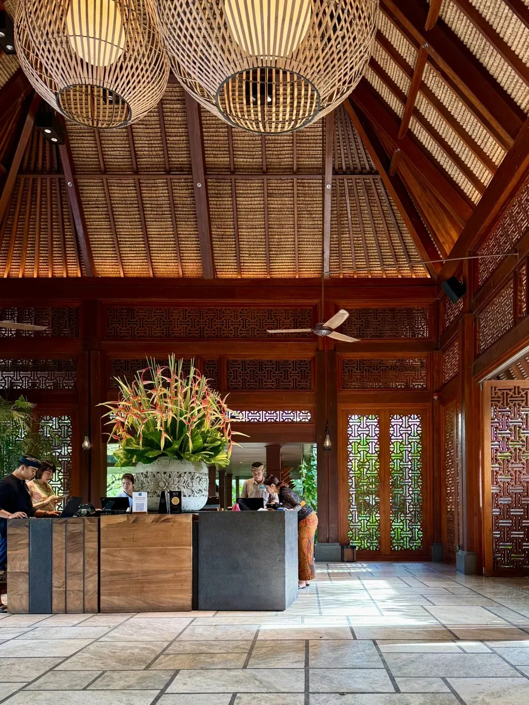 The lobby pavilion under a soaring thatched roof, with woven pendant lamps and carved timber screens
