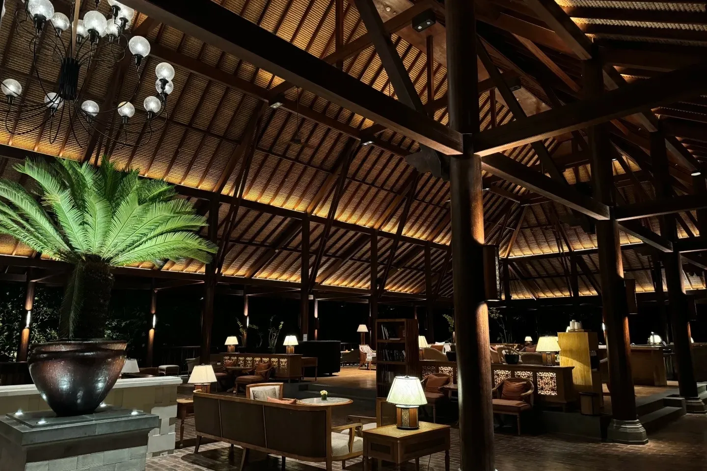 The lobby lounge under a soaring timber roof, with lamps, armchairs and a large cycad