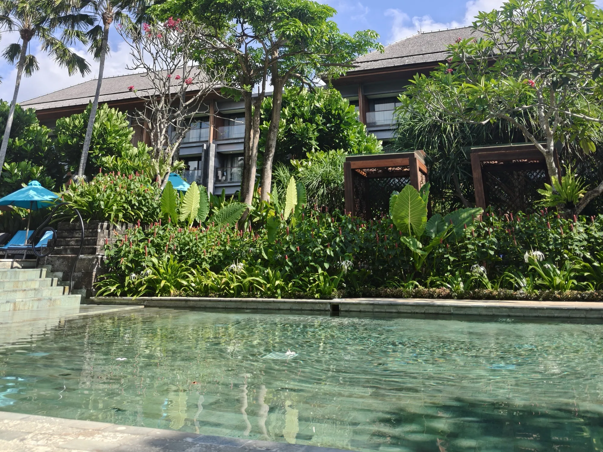 Clear green pool water in front of a tropical garden, timber cabanas and the guest-room wing