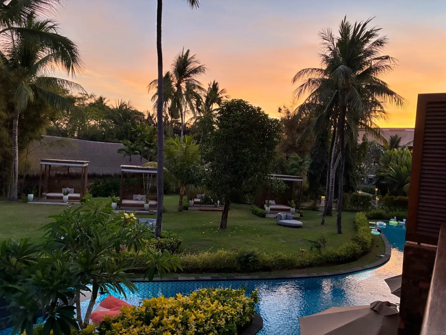 Pool, lawn and cabanas under coconut palms at sunset