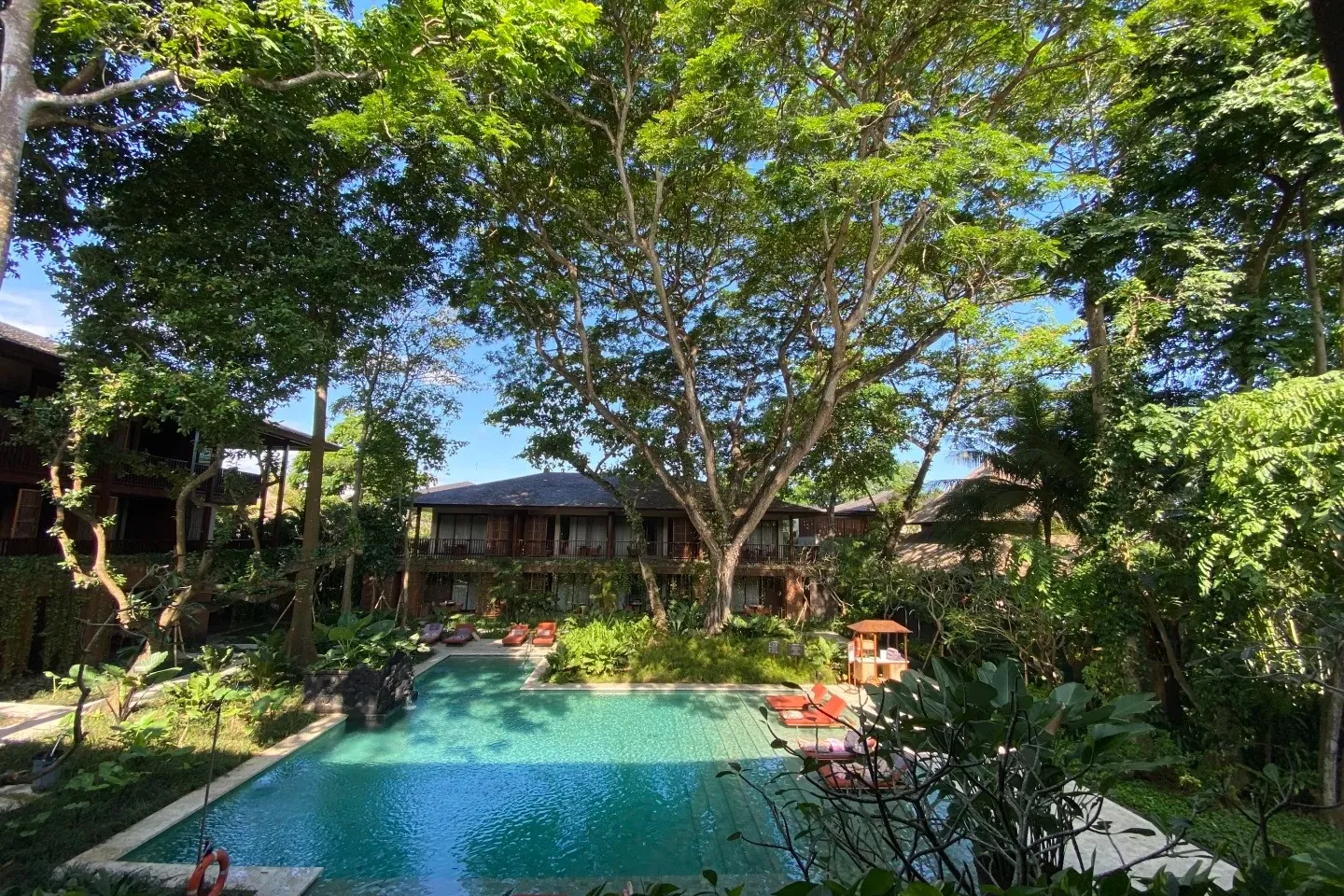 A pool in the gardens under big shade trees, with a guest wing behind