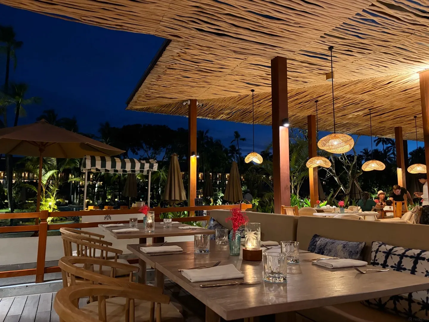 An open-air restaurant terrace under woven lampshades in the evening