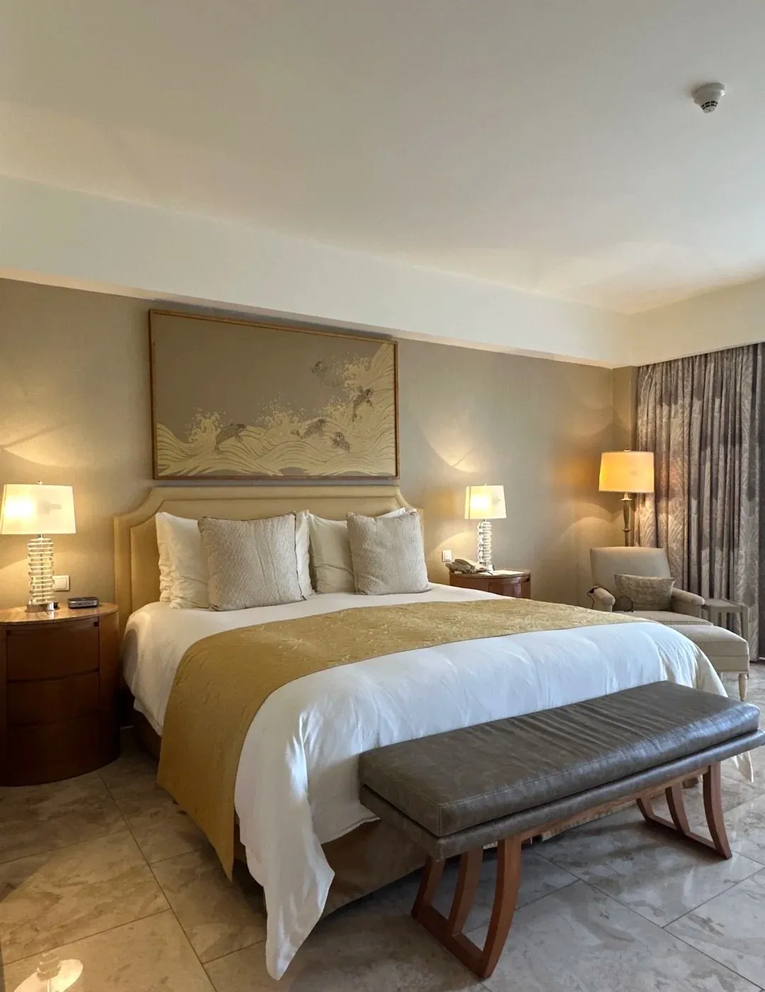 A king bed with a gold runner and a leather bench at its foot, under a koi wave print