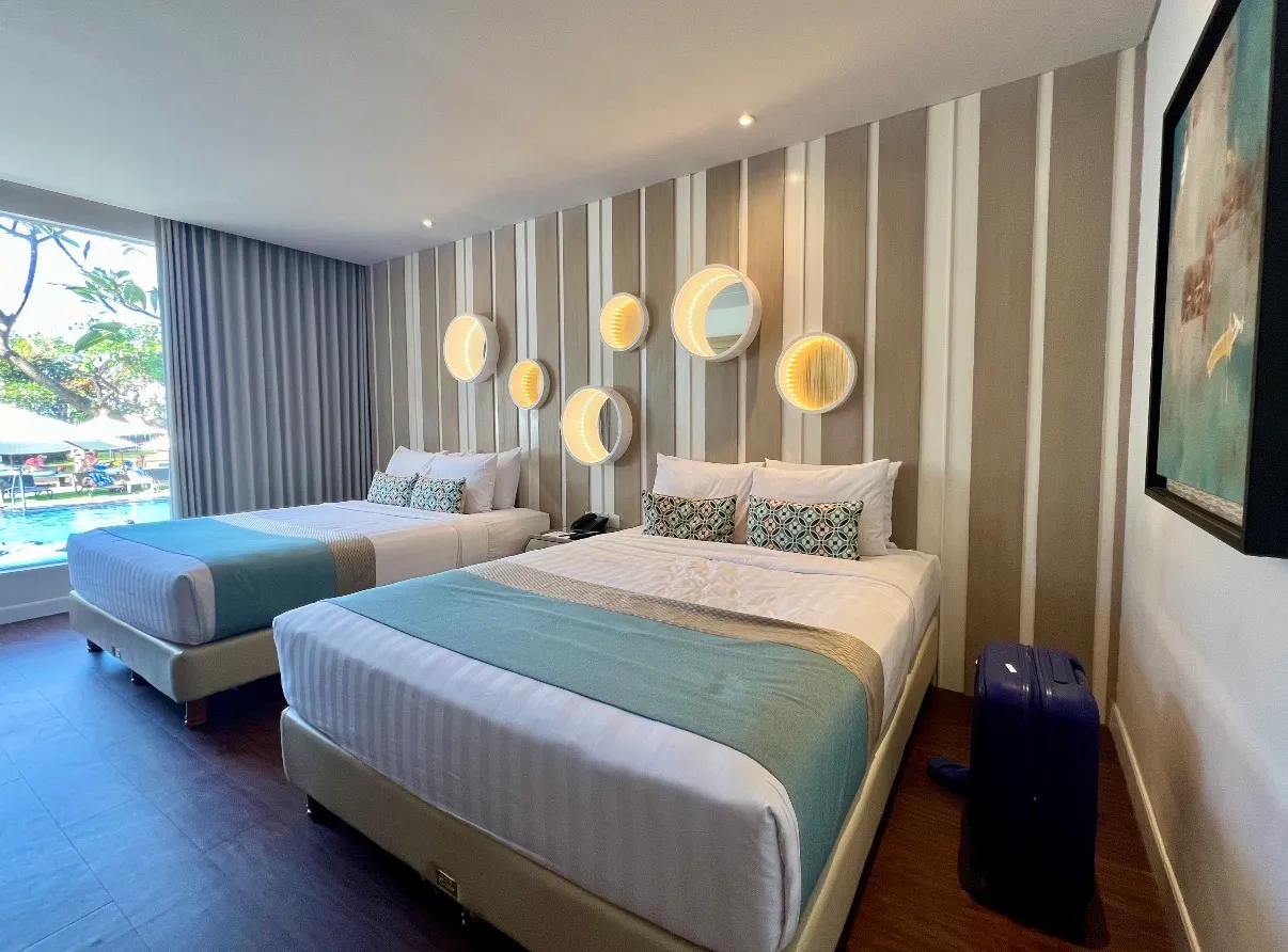A Grand Mirage room with two double beds, round lit mirrors on a striped wall and a window onto the pool