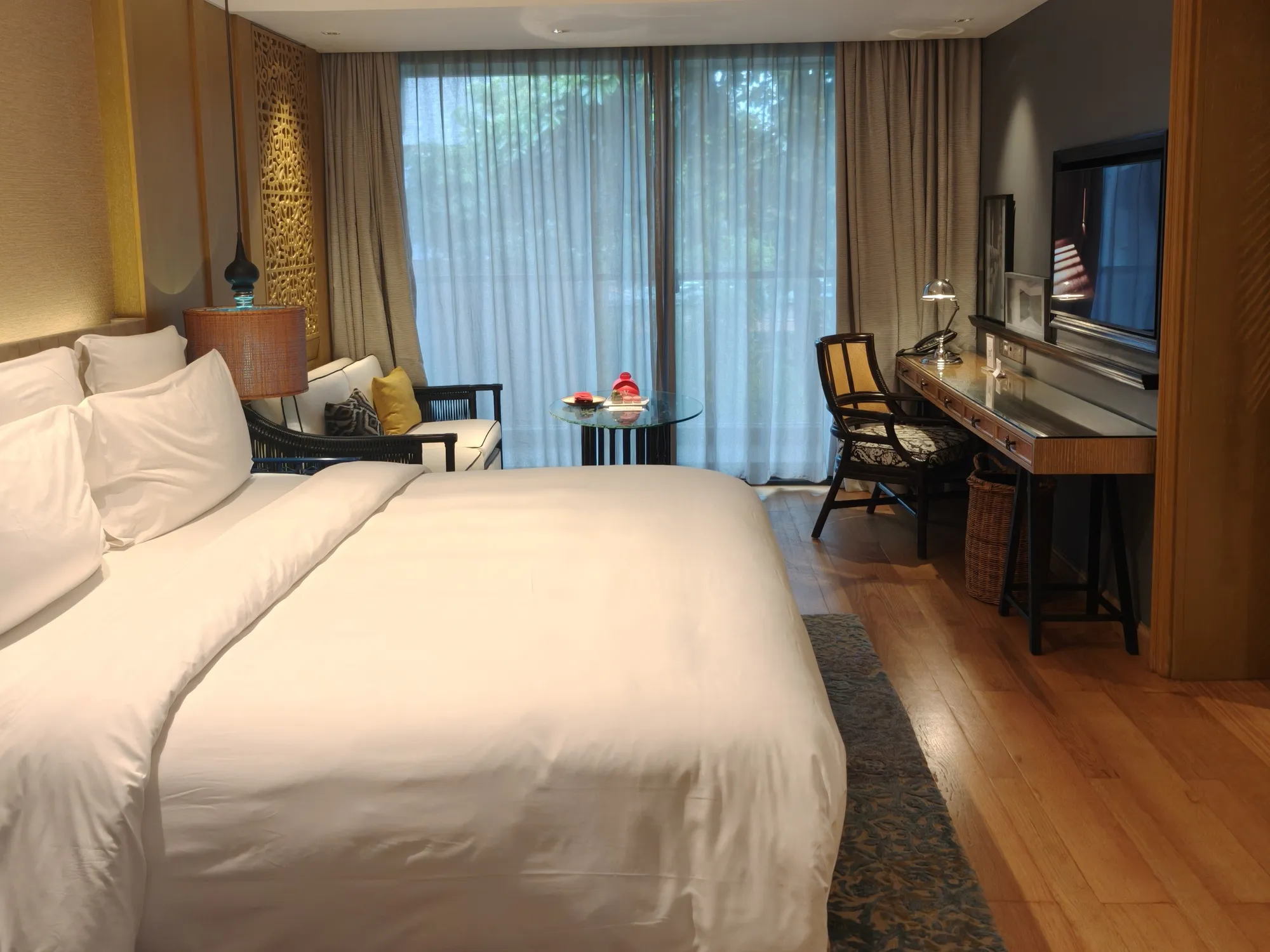 A Hotel Indigo room with a king bed, timber floors, a desk and sheer curtains over a balcony door
