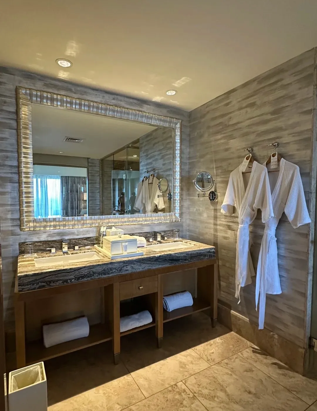 A double marble vanity with two white bathrobes hanging beside it
