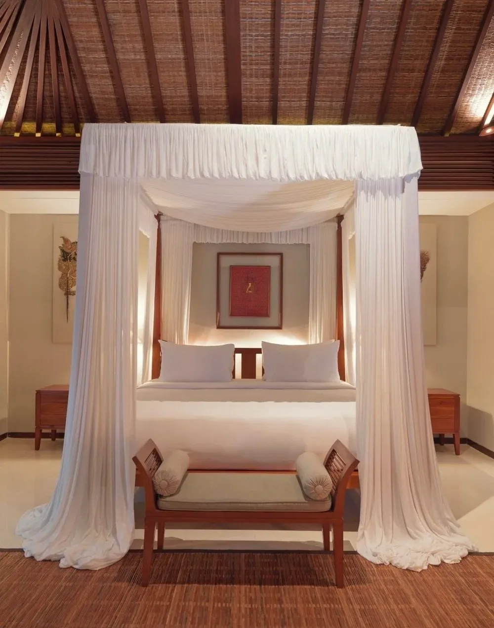 A villa bedroom with a four-poster bed draped in white curtains, under a timber roof